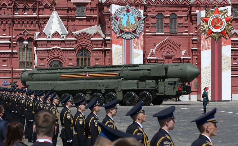 一枚俄罗斯核导弹在红砖建筑前的红场上滚动，两侧有军事人员