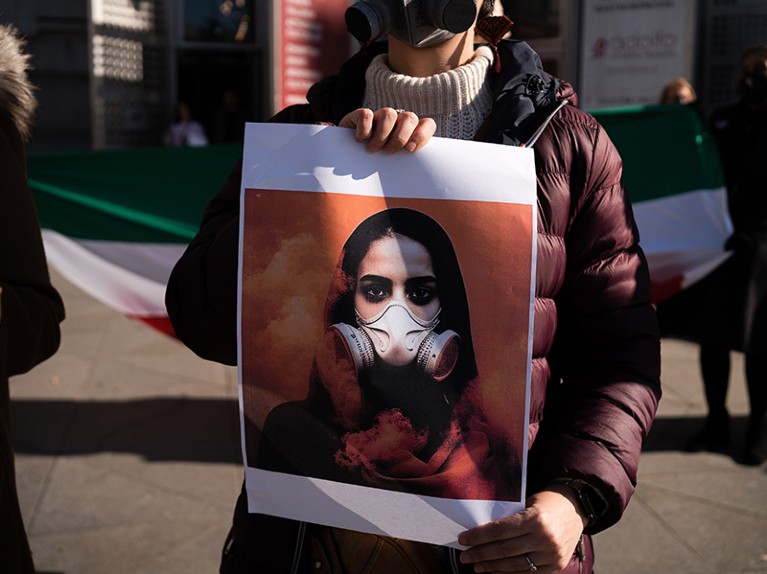 A woman holds a placard with a drawing of a girl wearing gas masks in Iran during the demonstration.