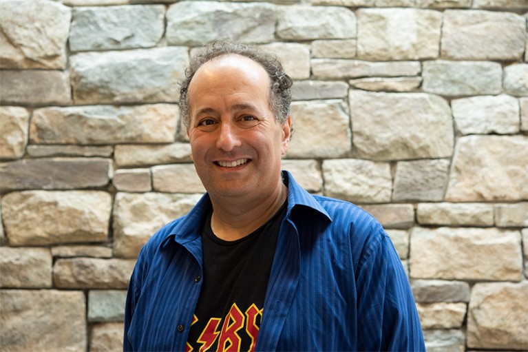 Michael Eisen shown smiling in an informal portrait, shot taken against a backdrop of a stone wall at HHMI campus