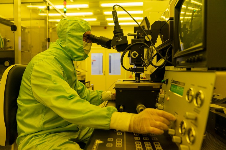 Luis Fonseca in full protective clothing in a clean room with yellow lighting. He is looking through a microscope
