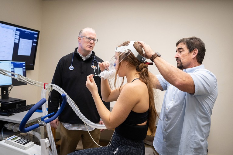 Todd Davenport and Mark Van Ness in a laboratory testing the fitness of a study participant with a respirator.