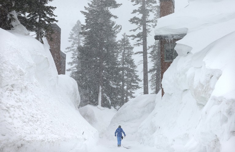 A person walks near snowbanks obscuring condominiums as snow falls in the Sierra Nevada mountains from yet another storm system.