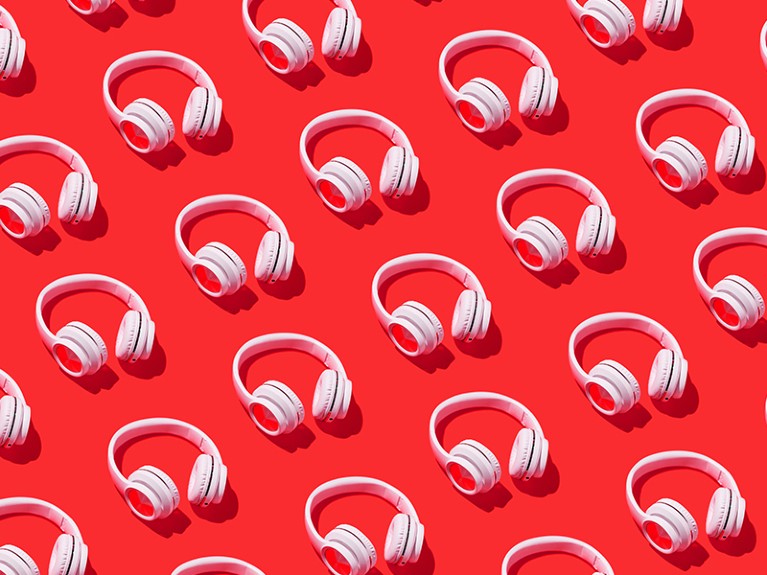 Pattern of white wireless headphones with hard shadow on red background.