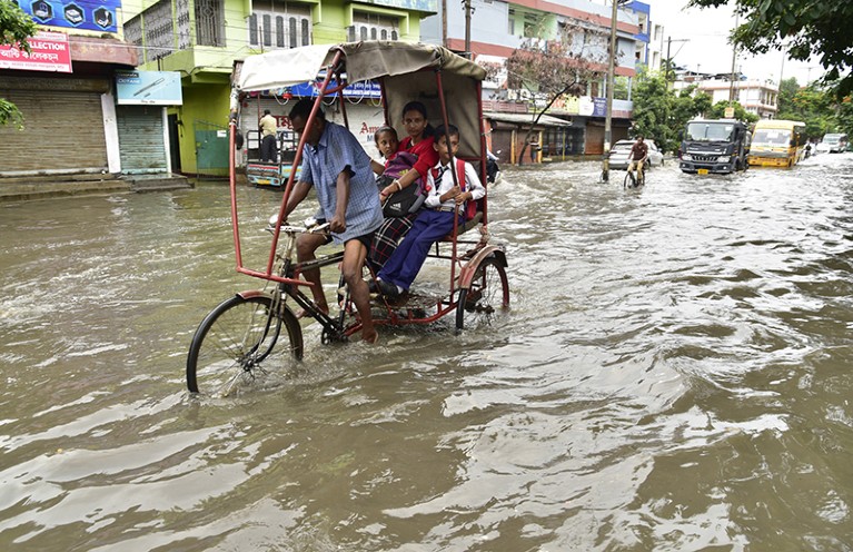 雨季期间，阿萨姆邦古瓦哈提，一名人力车夫带着他的乘客穿过被雨水浸湿的街道。