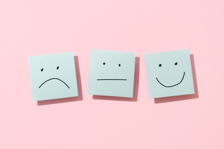 Three blue sticky notes with a sad, neutral and happy face on a pink background