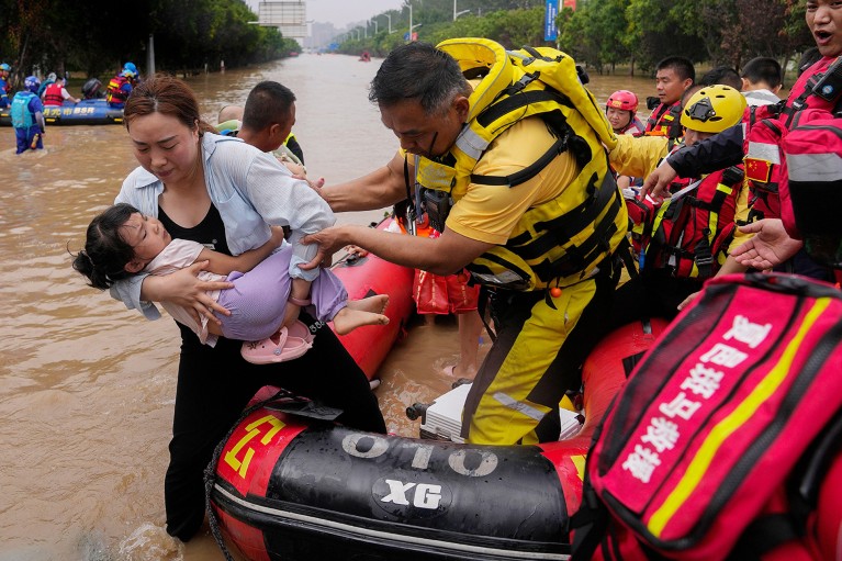 Woman and child step off rubber dinghy into brown floodwaters.