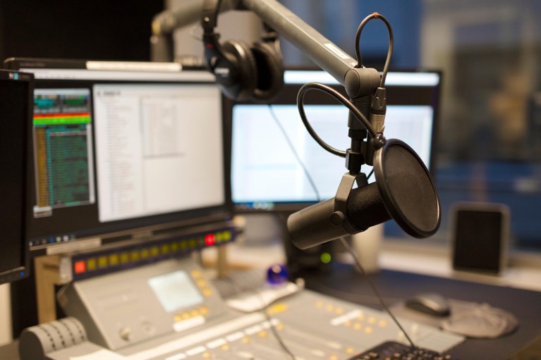 Close-up of a microphone in a radio broadcasting studio with computer screens in the background