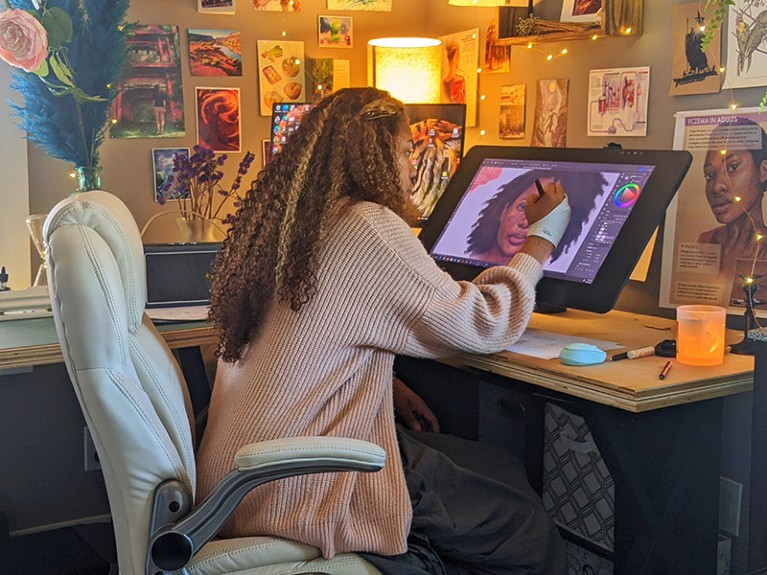 希拉里·威尔逊是坐在她的工作室在桌子上进行一项使用平板电脑她画插图。