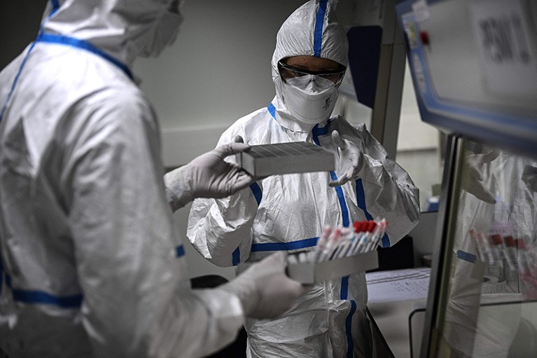 Laboratory technicians in protective gear handle samples of the SARS-CoV-2 virus.