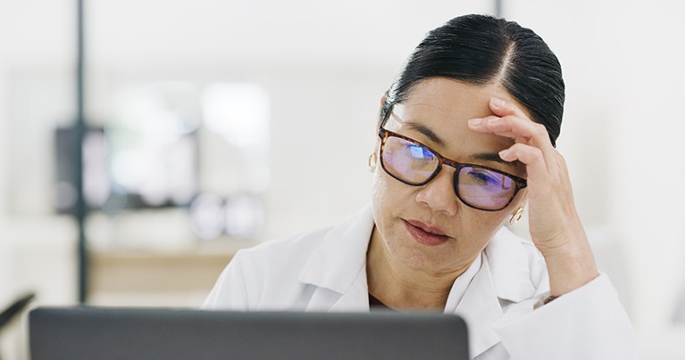 Female scientist looking tired reading risk report on computer