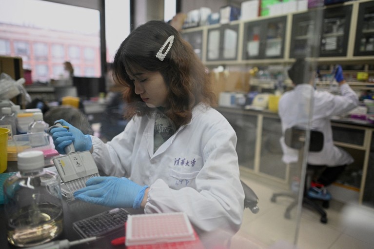 A laboratory technician wearing a white lab coat and blue gloves works at a Tsinghua University lab