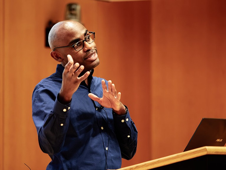 Neil Lewis gesturing with his hands during a talk at a conference