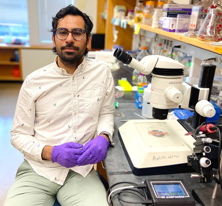 Portrait of Mayank Chugh next to a work bench in a lab with microscope and other science paraphernalia