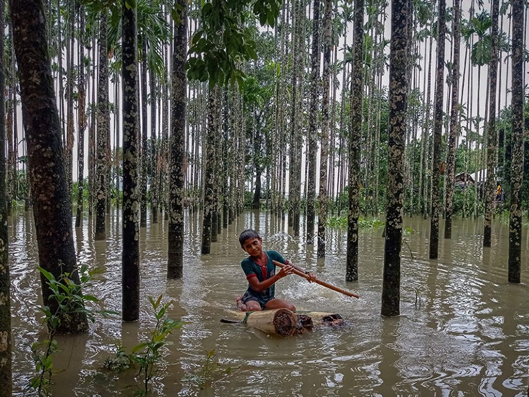 A child paddles through a flooded area using a makeshift raft at Maulovir Para, India.