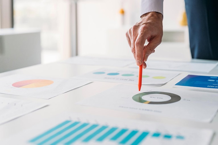 The hand of a businessman holding a pen and hovering above a doughnut chart printout on table.