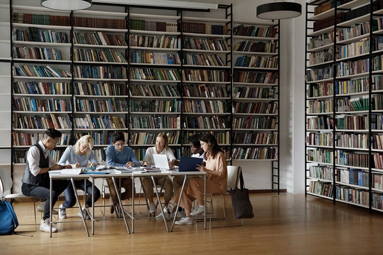 Group of multiracial students sit at table in library.