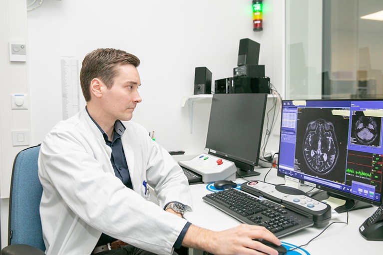 Juho Joutsa sits at a computer screen reviewing brain scan images.