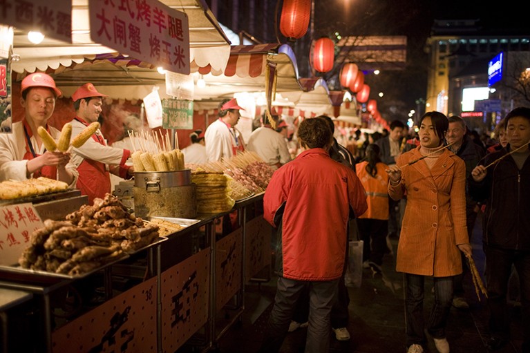 People walk past stalls selling meat kebabs and corn on the cobs in the Night Market, Wangfujing Street, Beijing