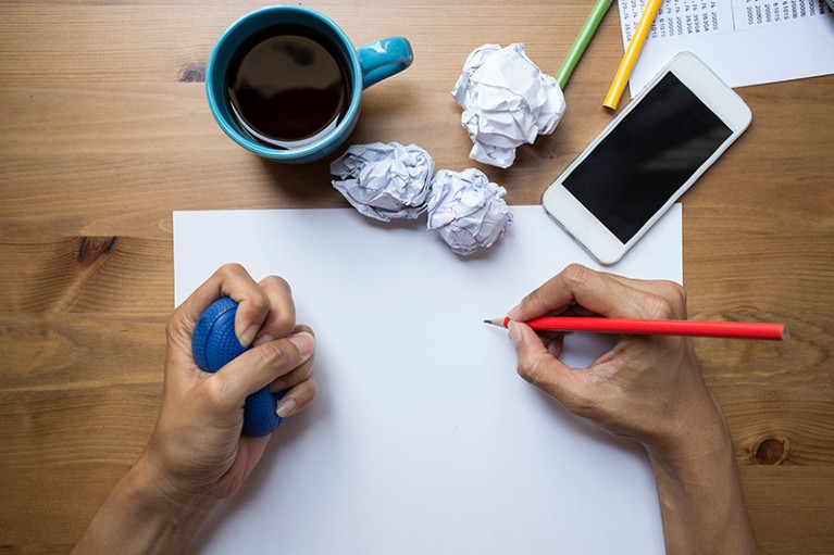 Top down view of a persons hands holding a pencil and stress ball in the process of rewriting a document.