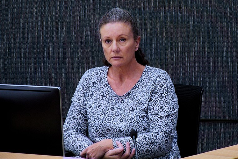 A woman sitting in a court dock with a microphone in front of her.