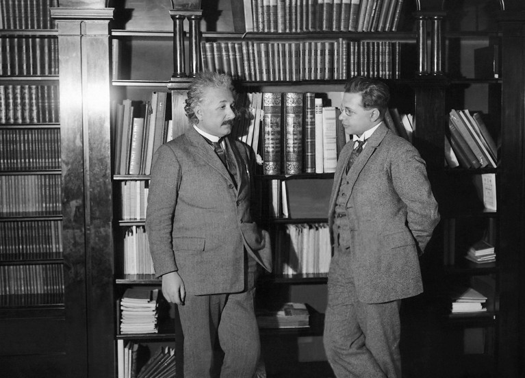 historical black and white photo of Albert Einstein talking with his son Hans in front of some bookshelves