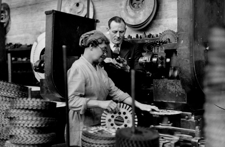 A vintage black and white image of a supervisor checking a female employee's performance against a stopwatch
