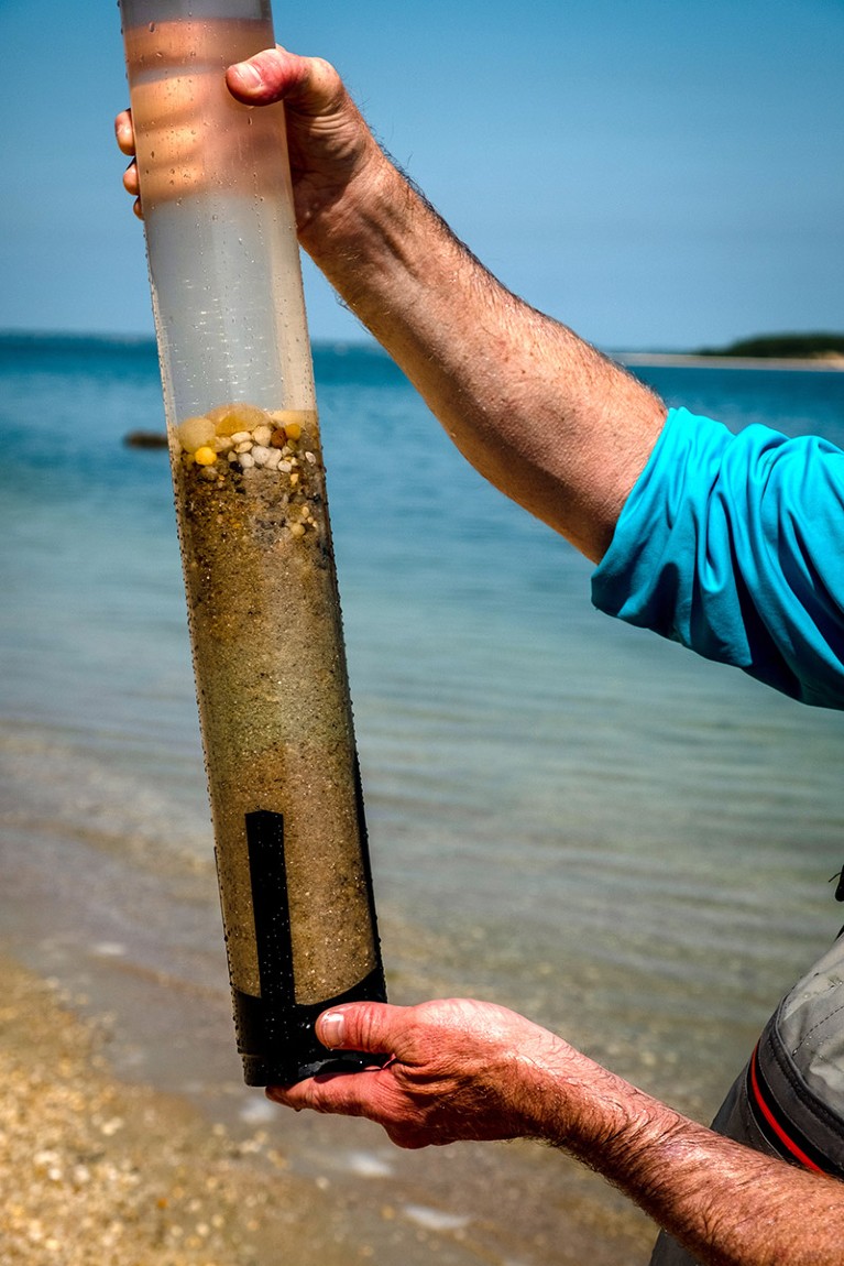 Man is holding a sediment collection tube. The olivine sand can be seen in the middle area