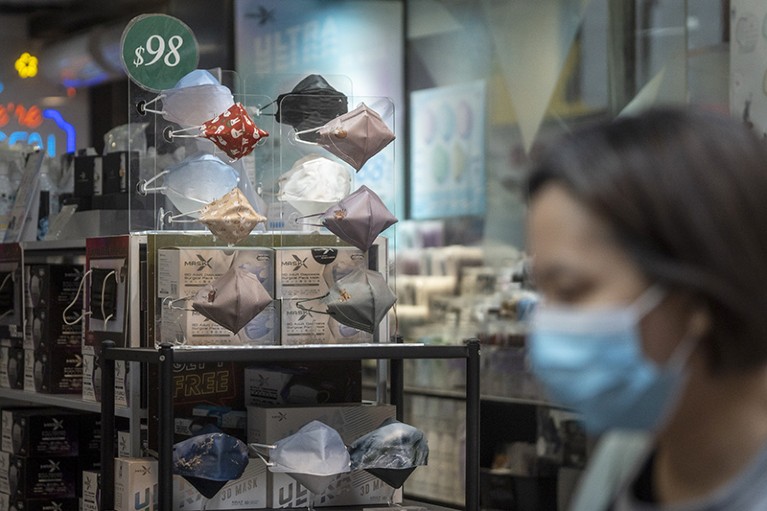 Face masks in shop display with blurred woman, wearing a mask, in the foreground.