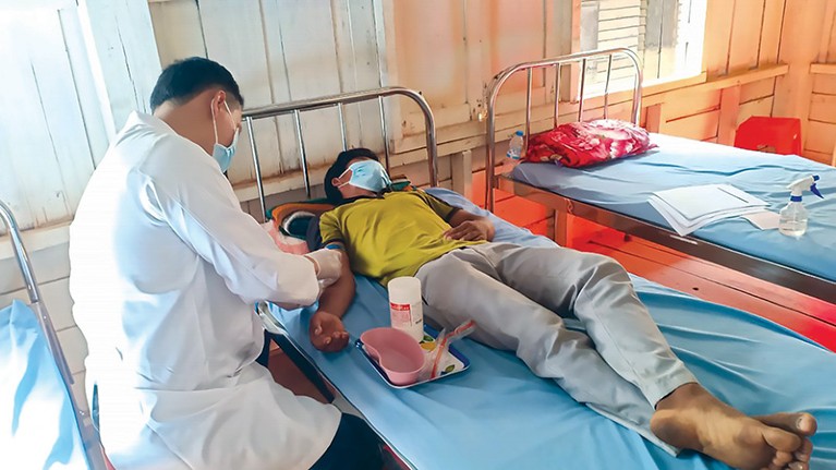 A nurse in a lab coat takes a blood sample from a patient lying in a hospital bed