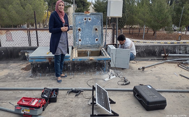 Esraa Tarawneh stands with equipment and tools nearby for installing a water-monitoring device.