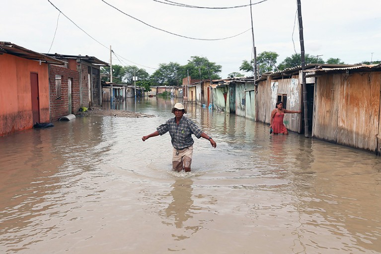 一个男人在秘鲁涉水穿过街道被淹没的住宅。