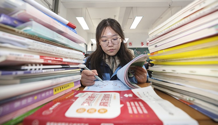 Student in the centre of the photo looking in a book, piles of books on either side