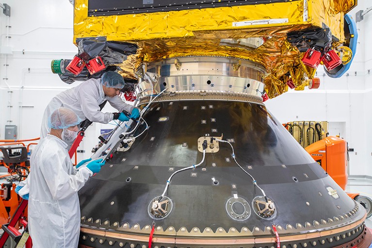 Two engineers in protective clothing work on spacecraft components.