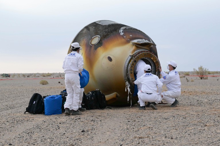 Employees assist colleagues out of the blackened return capsule of the Shenzhou-15 manned spaceship