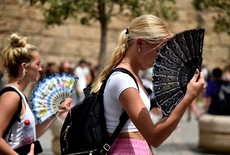 Two women use manual fans during a heatwave.