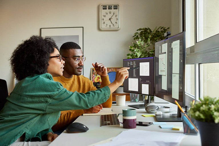 young multiracial woman discussing data on a computer monitor with a multiracial man in a home office