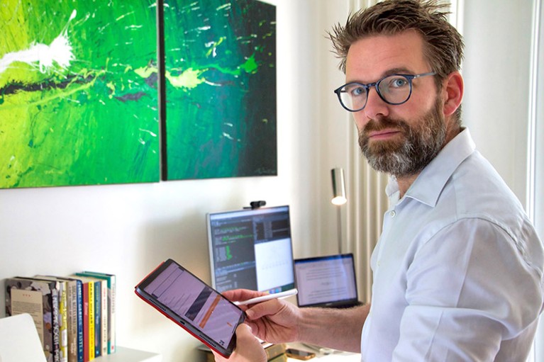Professor Theun Pieter Van Tienoven in his home office holding a tablet and with colourful canvas in background