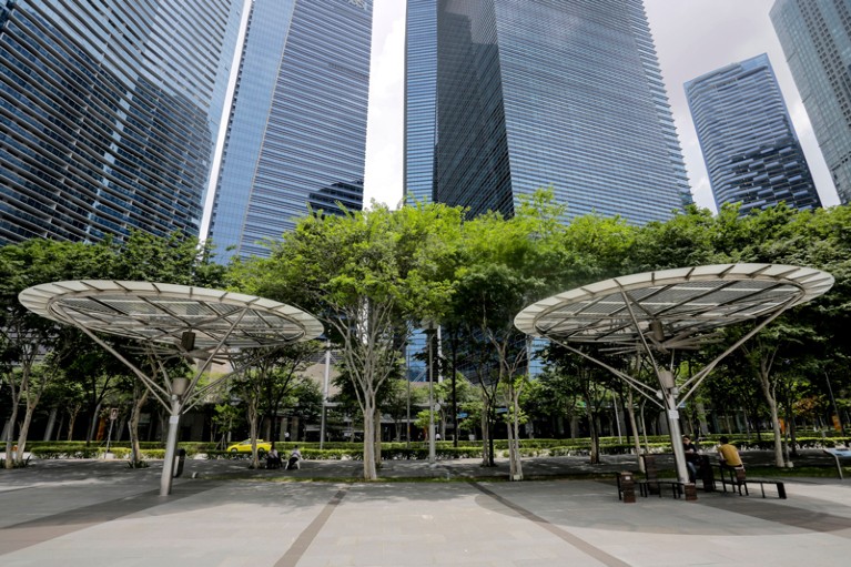 People rest under large circular shade structures in the financial district in Singapore