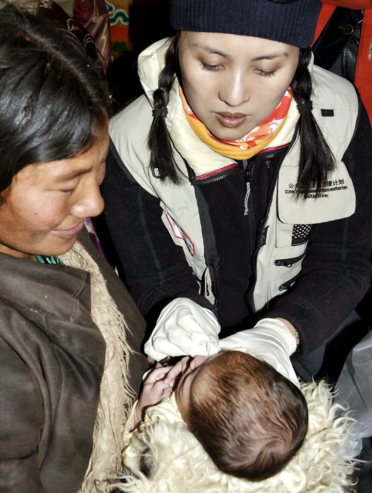 A woman holds a baby. The baby is being examined by Emily Chan.