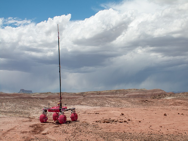 Pink robotic rover in desert landscape with grey clouds above.