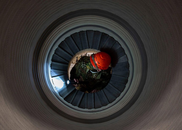 An aerospace propulsion technician with hardhat and torch is inspecting the seals inside the barrel on an aircraft engine