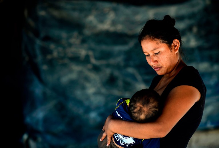 Indigenous Wichi woman stood breastfeeding her baby in her house