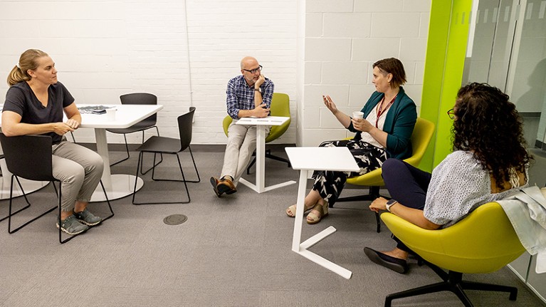 A group of four people sit on chairs chatting in a semicircle.