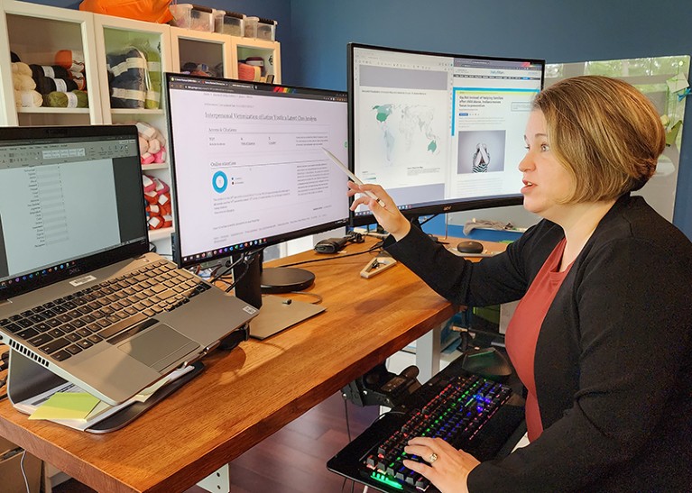 A women sits at a desk with multiple computer screens.