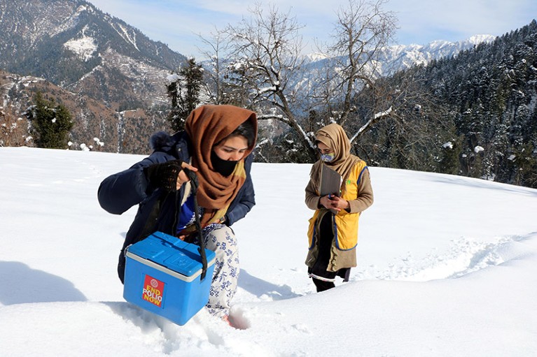 two female health workers hiking through snow with polio vaccine in the mountains of Pakistan