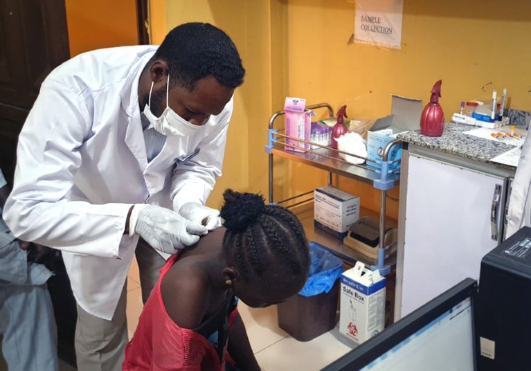 A doctor takes a skin sample from the back of a woman wearing a red top