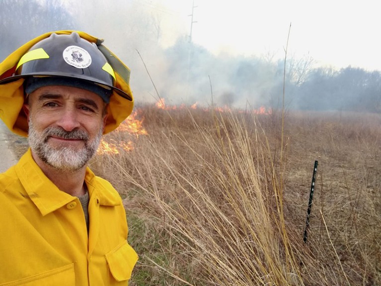 Andrew Stoehr in fire protective gear near a brush fire in a field.
