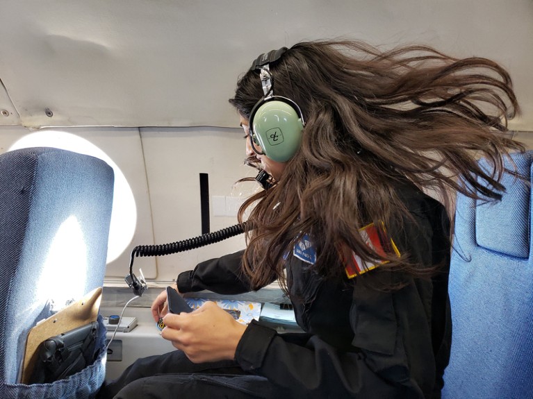 A woman in headphones works in an aeroplane seat, her long hair floating.