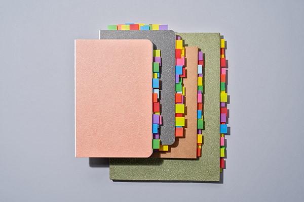 A stack of notebooks in which pages have been marked with many colourful post-it notes.