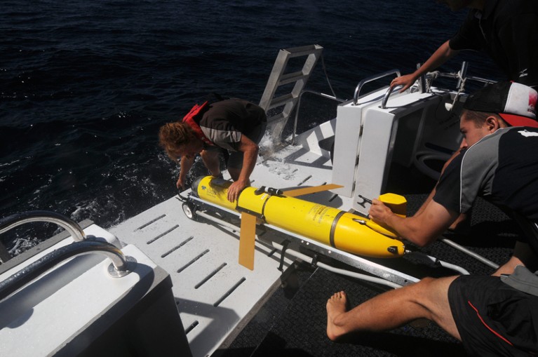 Two people deploy a slocum seaglider into the Indian Ocean off the back of a boat